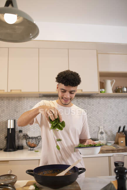 Усміхнений молодий чоловік готує зі свіжим базиліком на кухні — стокове фото