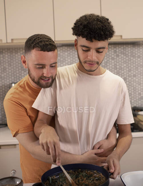 Прихильна пара гей-чоловіків готує і обіймає на кухні — стокове фото