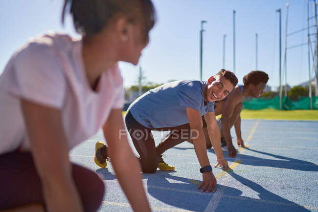 Corredores felizes na linha de partida na pista de esportes ensolarados — Fotografia de Stock