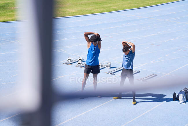 Male runners stretching on sunny blue sports track — Stock Photo