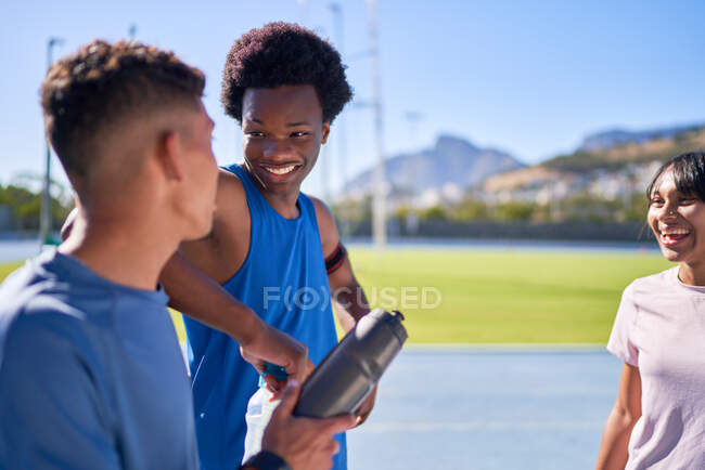 Jovens atletas felizes conversando na pista de esportes ensolarada — Fotografia de Stock