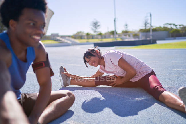 Happy young runners stretching on sunny sports track — Stock Photo