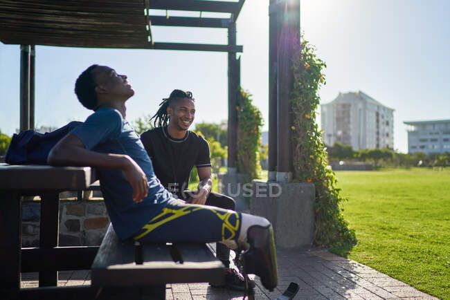 Atleta amputato e allenatore su panchina soleggiata del parco — Foto stock