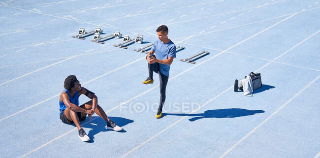Young male runners on sunny blue sports track — Stock Photo