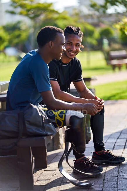 Male amputee athlete and coach talking on bench — Stock Photo