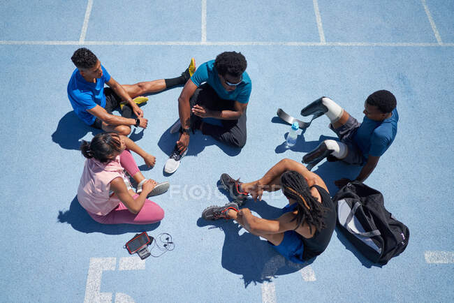 Jóvenes atletas hablando en pista de deportes azul soleado - foto de stock