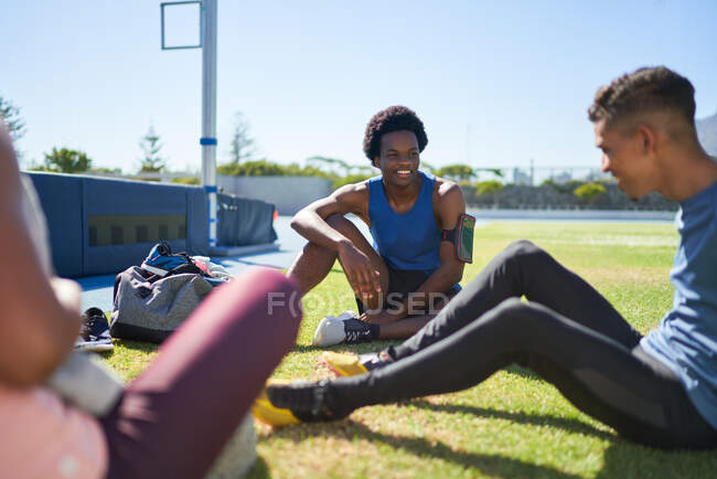 Male runners resting and talking on sunny field — Stock Photo