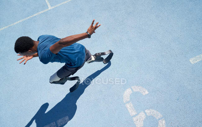 Male amputee athlete running on sunny blue sports track — Stock Photo