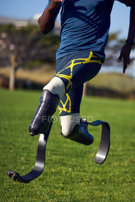 Male amputee athlete sprinting on sunny grass — Stock Photo