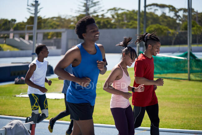 Sonrientes atletas de pista y campo corriendo en pista deportiva soleada - foto de stock