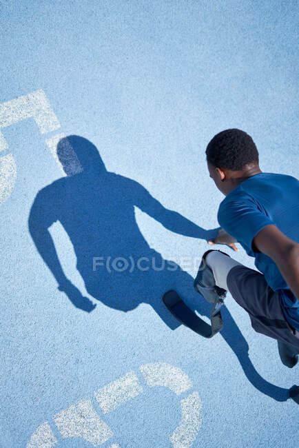 Jeune homme amputé sprinter prêt sur piste de sport bleu ensoleillé — Photo de stock