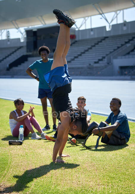 Athlete friends watching young man doing handstand in stadium — Stock Photo