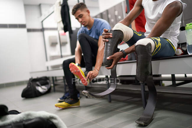 Спортсмен-ампутант регулирует протез бегущего лезвия в раздевалке — стоковое фото