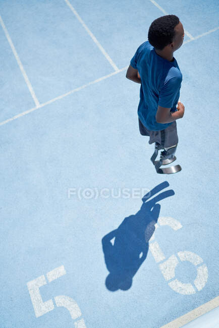 Jeune athlète amputé masculin s'échauffant sur une piste de sport ensoleillée — Photo de stock