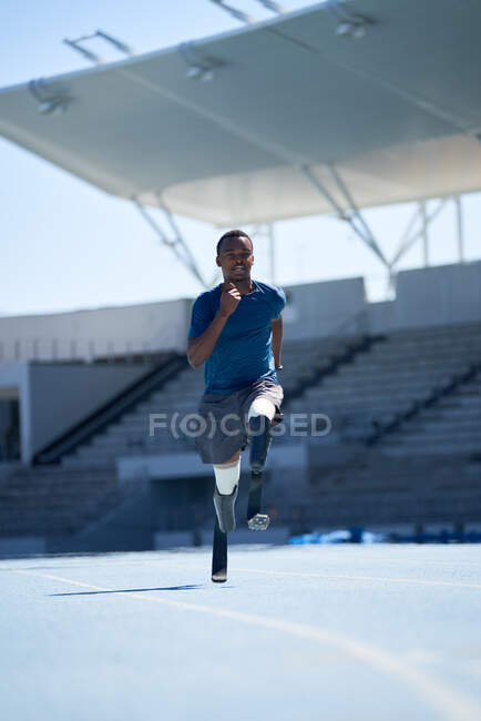Jovem atleta amputado masculino correndo na pista de esportes azul ensolarado — Fotografia de Stock