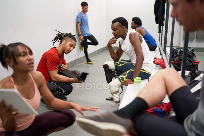Coach with running blade prosthetic talking to athlete in locker room — Stock Photo