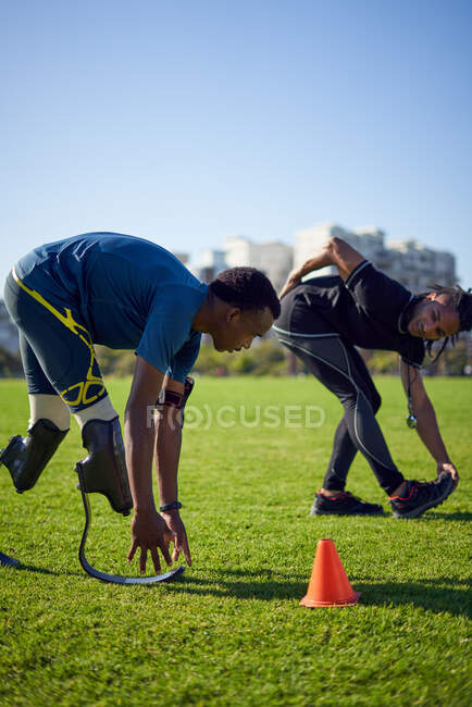 Coach and young male amputee athlete stretching in sunny park — Stock Photo