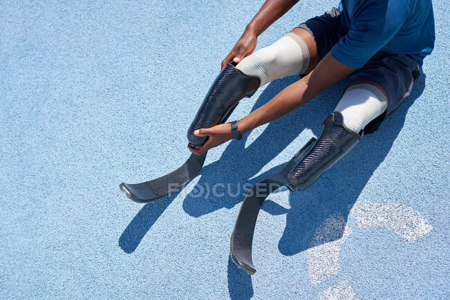 Male amputee athlete adjusting running blade prosthetic on blue track — Stock Photo