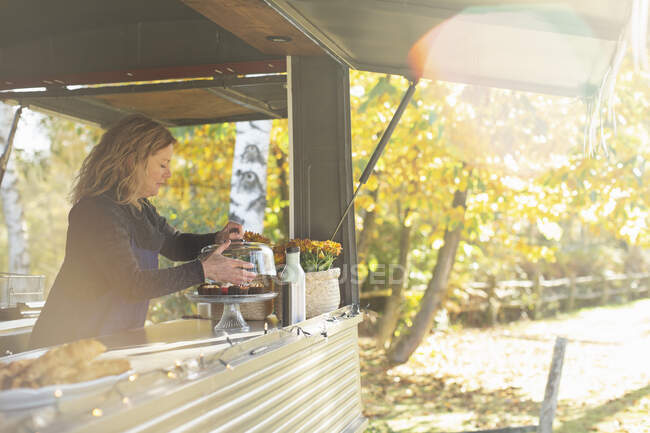 Female food truck owner arranging pastries in sunny autumn park — Stock Photo