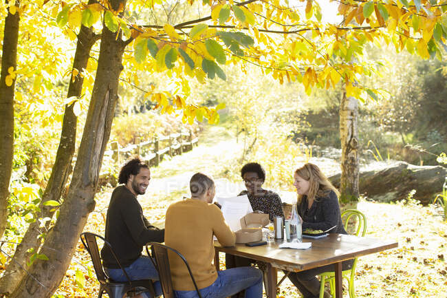 Творческая бизнес-команда собирается за столом в солнечном идиллическом осеннем парке — стоковое фото