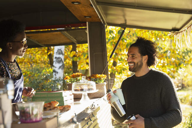 Счастливый клиент разговаривает с владельцем продуктового картона в осеннем парке — стоковое фото