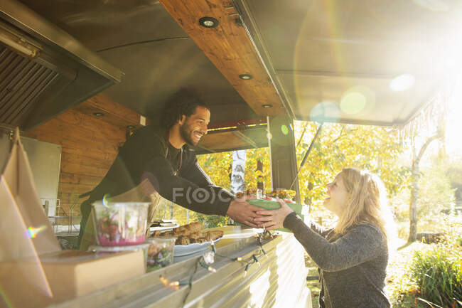 Joyeux propriétaire de camion de nourriture servant de la nourriture au client dans un parc ensoleillé — Photo de stock