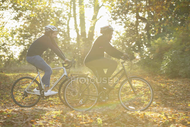 Couple bike riding through autumn leaves in sunny park — Stock Photo