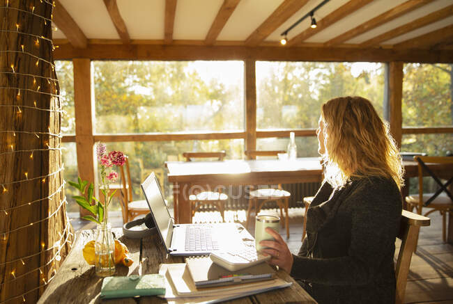 Thoughtful businesswoman working at laptop in sunny restaurant — Stock Photo