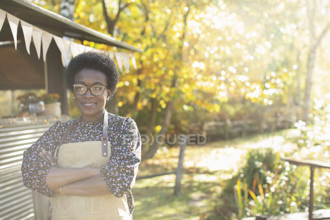 Propietaria de carrito de comida femenina con confianza en retratos en el soleado parque de otoño - foto de stock