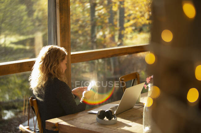 Femme d'affaires avec téléphone intelligent travaillant dans un café ensoleillé — Photo de stock
