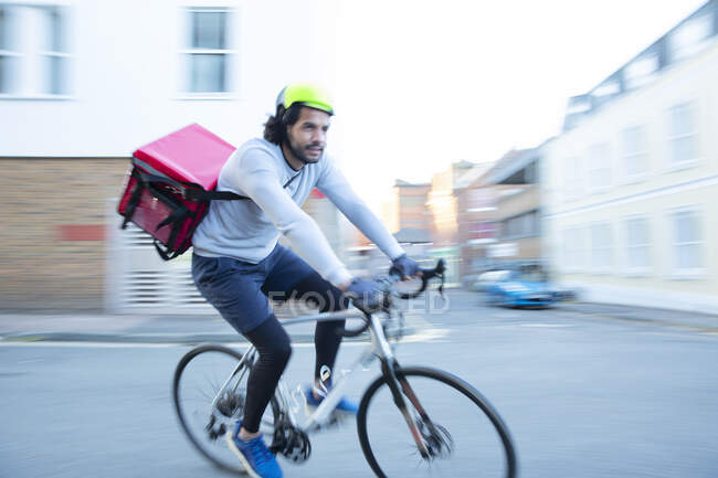 Messager à vélo mâle livrant de la nourriture à vélo dans le quartier urbain — Photo de stock