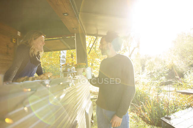 Proprietario di camion di cibo e cliente che parla nel soleggiato parco autunnale — Foto stock