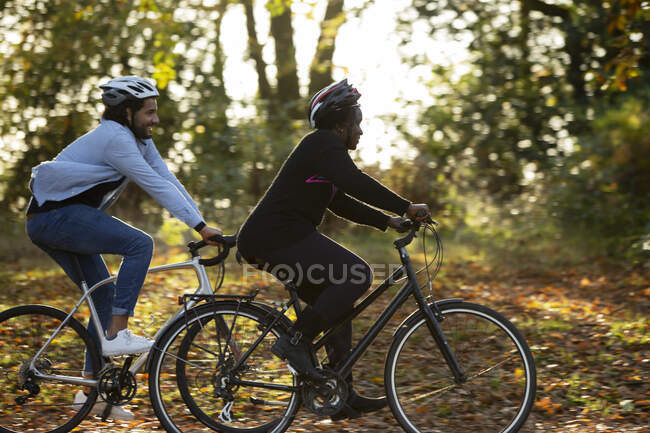 Friends riding bicycles through autumn leaves in park — Stock Photo