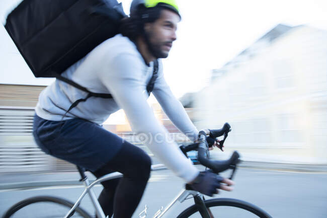 Mensageiro de bicicleta masculino entregando excesso de velocidade de comida na estrada — Fotografia de Stock
