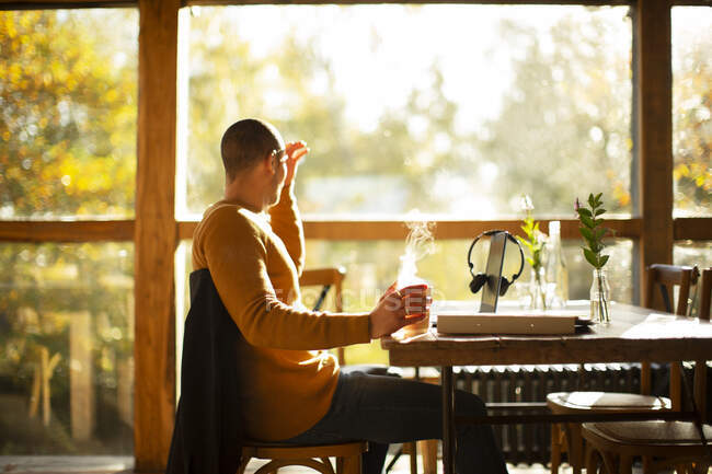 Бизнесмен с горячим кофе работает за столом в солнечном осеннем кафе — стоковое фото