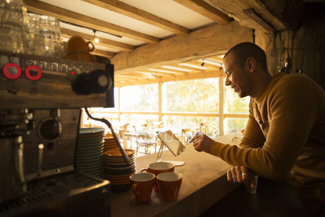 Männlicher Café-Besitzer nutzt digitales Tablet hinter Theke — Stockfoto