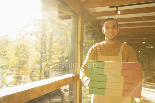 Retrato orgulhoso proprietário pizzaria masculino com caixas de pizza na janela ensolarada — Fotografia de Stock