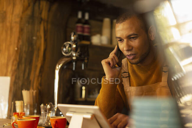 Чоловік власник кафе приймає замовлення по телефону на цифровому планшеті — стокове фото