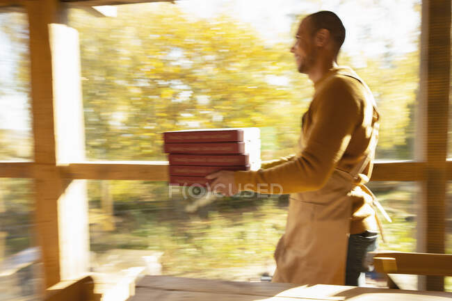 Владелец мужской пиццерии несет коробки с пиццей вдоль солнечного осеннего окна — стоковое фото