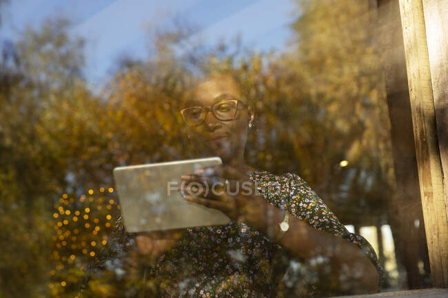 Женщина за цифровым планшетом у окна с отражением осенних деревьев — стоковое фото