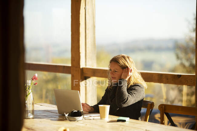 Businesswoman working at laptop at sunny cafe table — Stock Photo