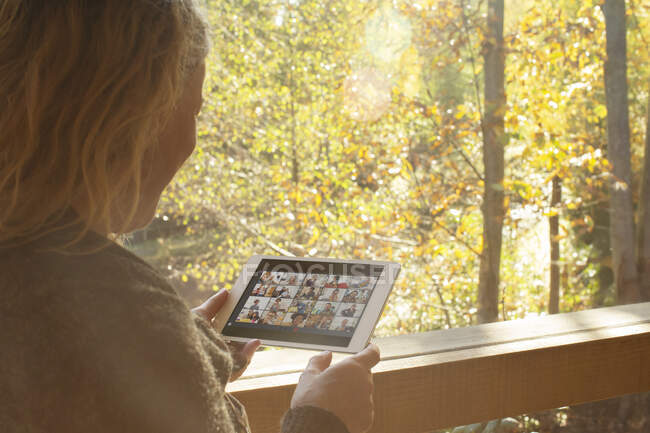 Mujer vídeo chat con amigos en la tableta digital en la ventana de otoño - foto de stock