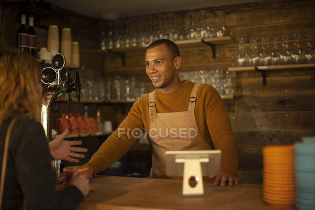 Amistoso camarero hablando con el cliente en el mostrador de la cafetería - foto de stock