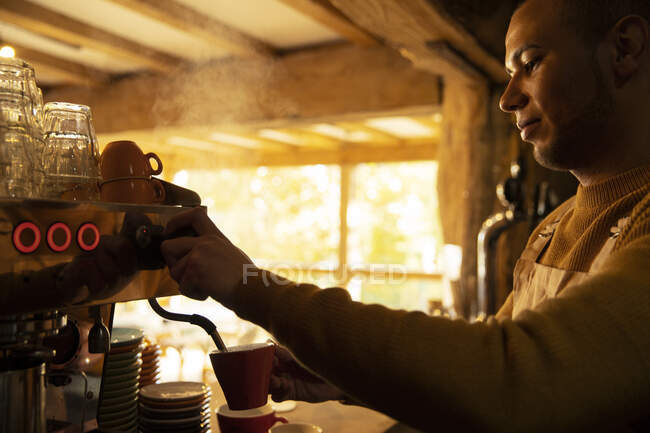 Varón barista preparando capuchino en la máquina de café expreso en la cafetería - foto de stock