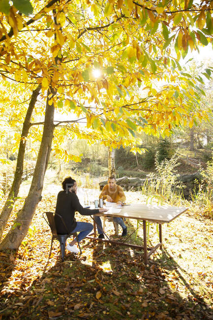 Hommes d'affaires travaillant à table dans un parc d'automne idyllique ensoleillé — Photo de stock