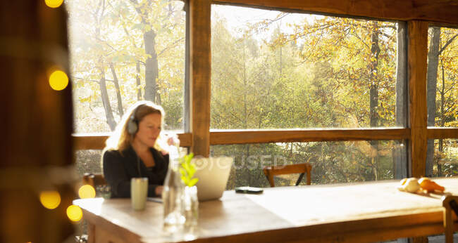 Donna d'affari con cuffie che lavorano al computer portatile nel soleggiato caffè autunnale — Foto stock