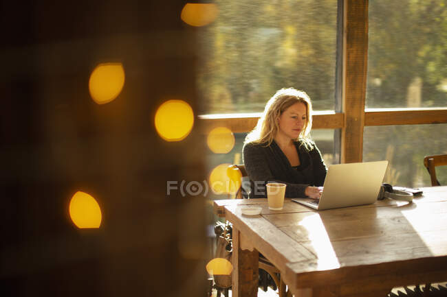 Femme d'affaires travaillant à l'ordinateur portable dans un café ensoleillé — Photo de stock