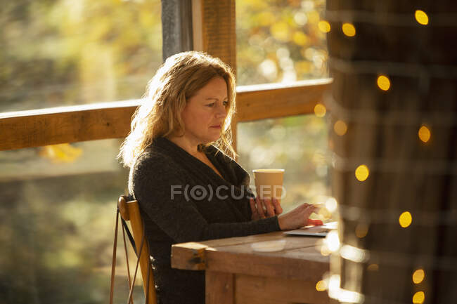 Femme d'affaires ciblée avec café travaillant dans un café ensoleillé — Photo de stock