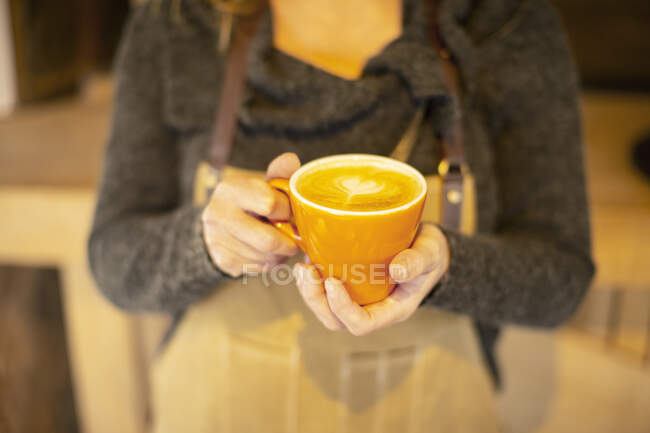 Cerca de barista hembra celebración cappuccino con espuma del corazón - foto de stock