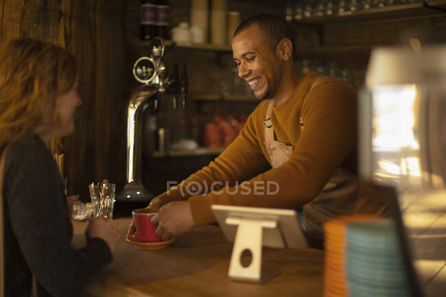 Friendly barista serving coffee to excited woman at cafe counter — Stock Photo